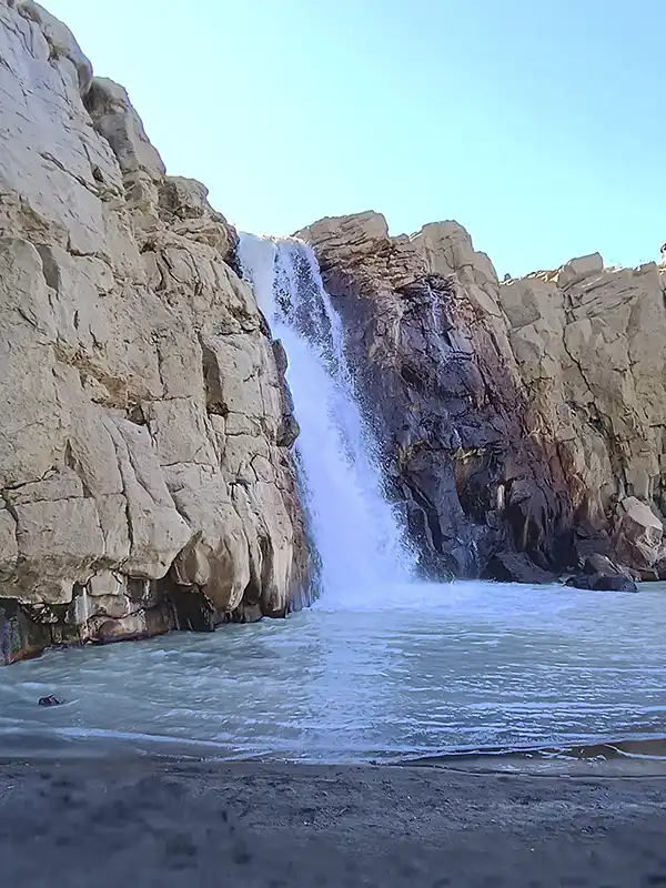 Primer plano de una cascada de agua blanca cayendo entre paredes de roca basáltica de tonos ocres y marrones en Caviahue.