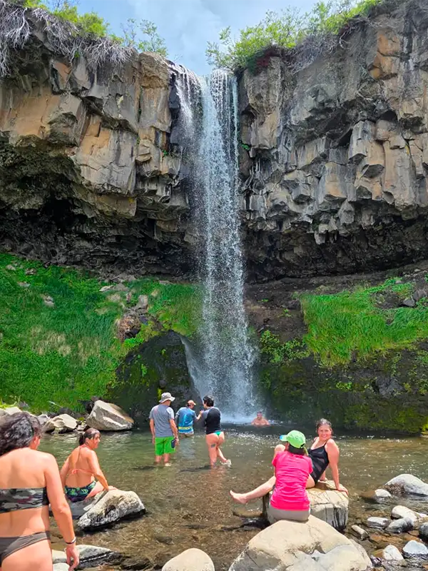 Grupo de turistas relajándose y bañándose en las aguas cristalinas al pie de una cascada durante una tarde de verano en Caviahue con Vivak Aventuras.