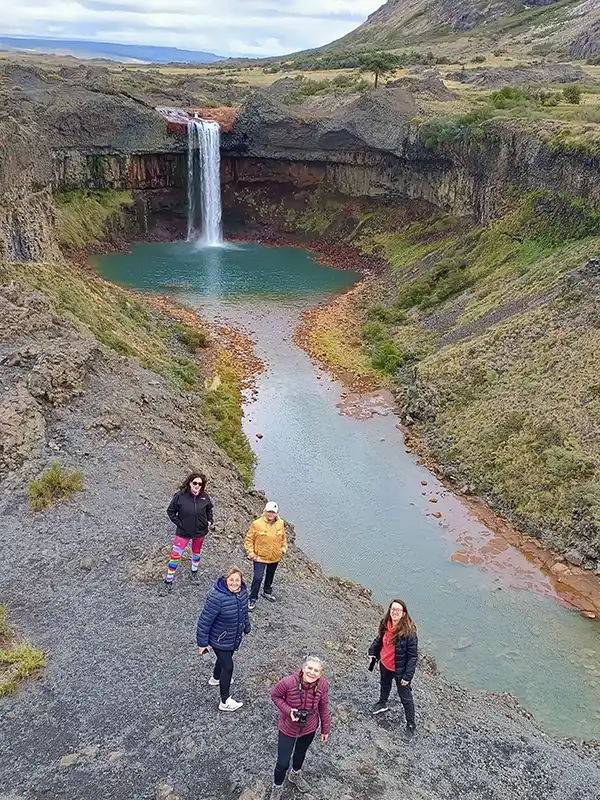 Grupo de turistas descansando en un mirador con pehuenes, observando el lago turquesa y el pueblo de Caviahue durante una excursión guiada.