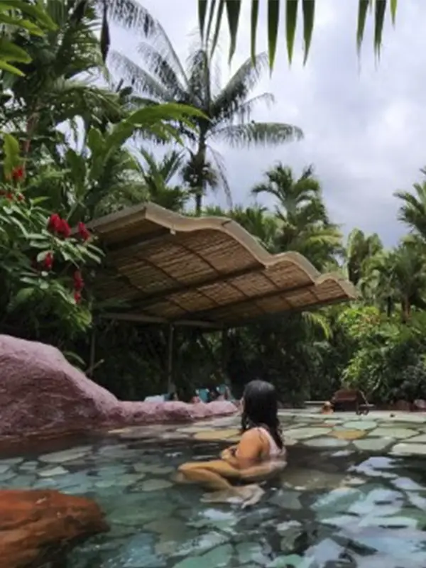 Turista relajándose en las aguas termales rodeadas de vegetación tropical en Arenal, Costa Rica