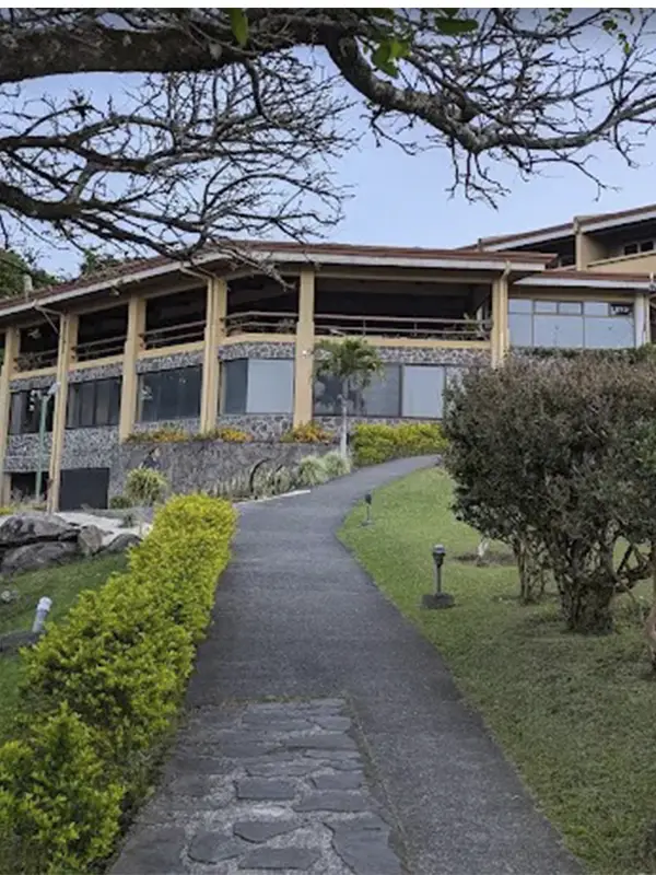 Vista exterior de la estructura de piedra y balcones del Hotel Montaña Monteverde, rodeado de cuidados jardines y árboles.