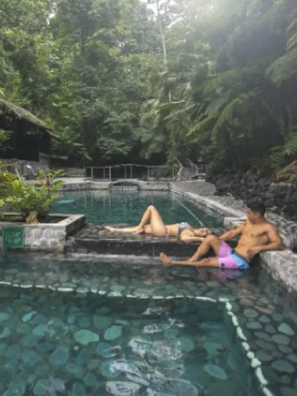 Pareja relajándose en piscinas de aguas termales oscuras rodeados de un frondoso bosque tropical.