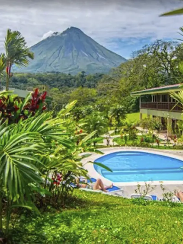 Pareja relajándose en reposeras junto a la piscina del hotel rodeada de naturaleza y con vistas al Volcán Arenal.