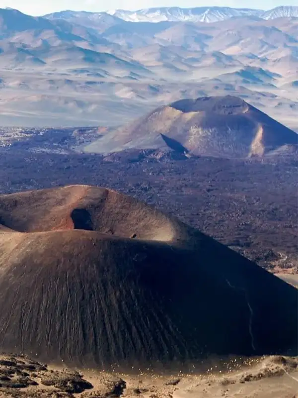 Vista aérea de los conos volcánicos del Antofagasta en Catamarca, mostrando el contraste entre la lava negra y las cumbres rojizas bajo un cielo despejado.