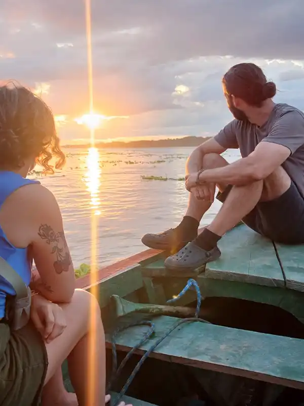 Un viajero de espaldas en una embarcación de madera contemplando la majestuosa salida del sol sobre las aguas del río Amazonas, rodeado por la silueta de la selva.