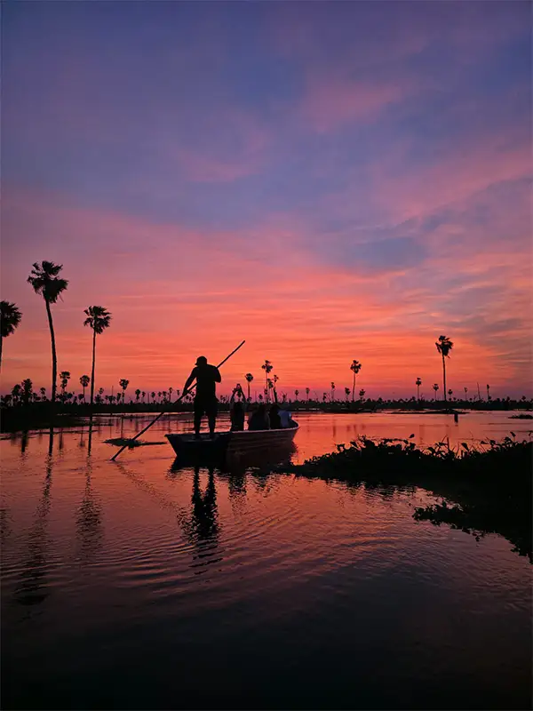 Silueta de un balsero guiando una canoa con viajeros bajo un cielo rojizo al atardecer en el Bañado La Estrella — la imagen más icónica del humedal formoseño.