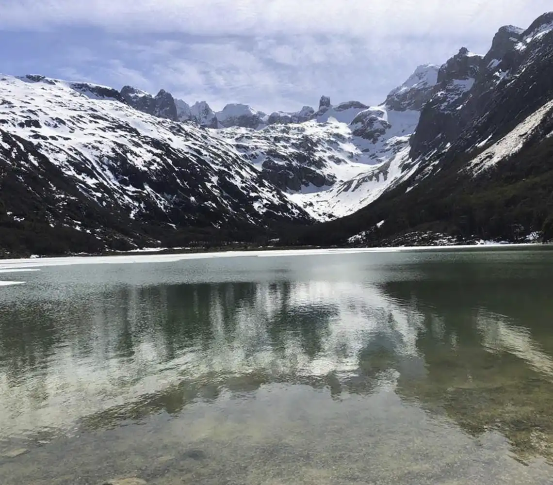 Vista de picos nevados de la Cordillera de los Andes sobre un lago calmo durante el día en Ushuaia.