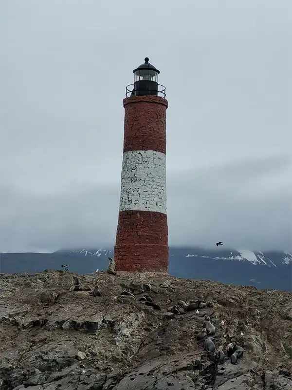 El histórico Faro Les Eclaireurs pintado de rojo y blanco sobre un islote rocoso, rodeado de lobos marinos en el Canal Beagle, Ushuaia.