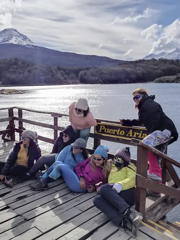 Grupo de viajeras posando en el muelle de Puerto Aria, cartel del fin de la Ruta Nacional 3, Parque Nacional Tierra del Fuego, Ushuaia.