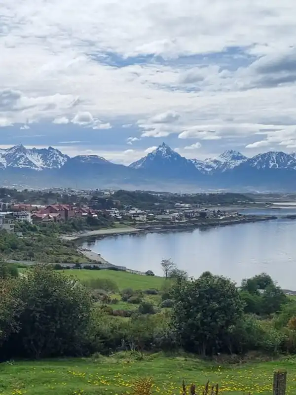 Vista panorámica de la ciudad de Ushuaia y su bahía desde la altura, con la imponente Cordillera de los Andes nevada de fondo.