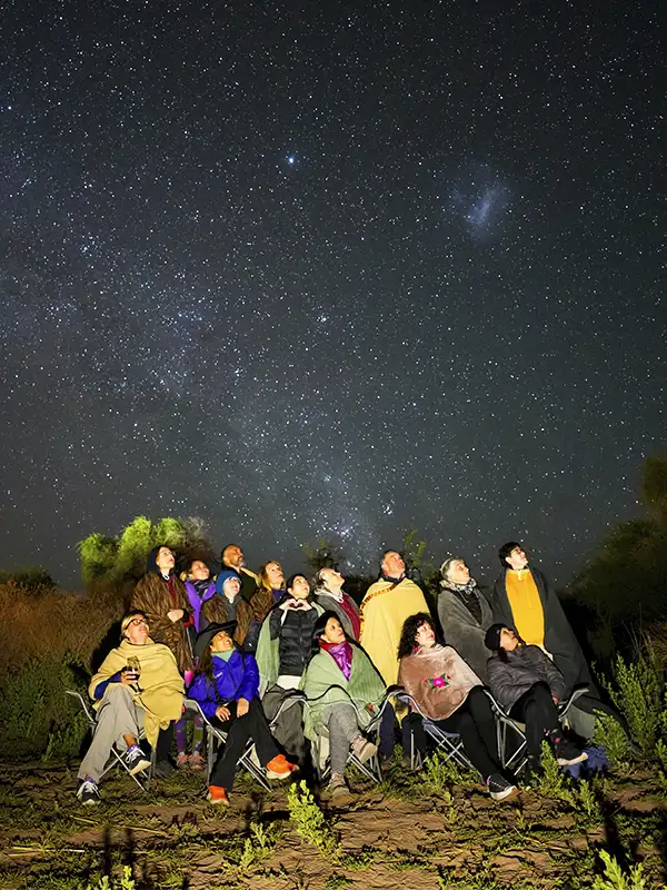 Grupo de viajeros recostados en sillas contemplando el cielo estrellado durante una noche de astroturismo en San Pedro de Atacama