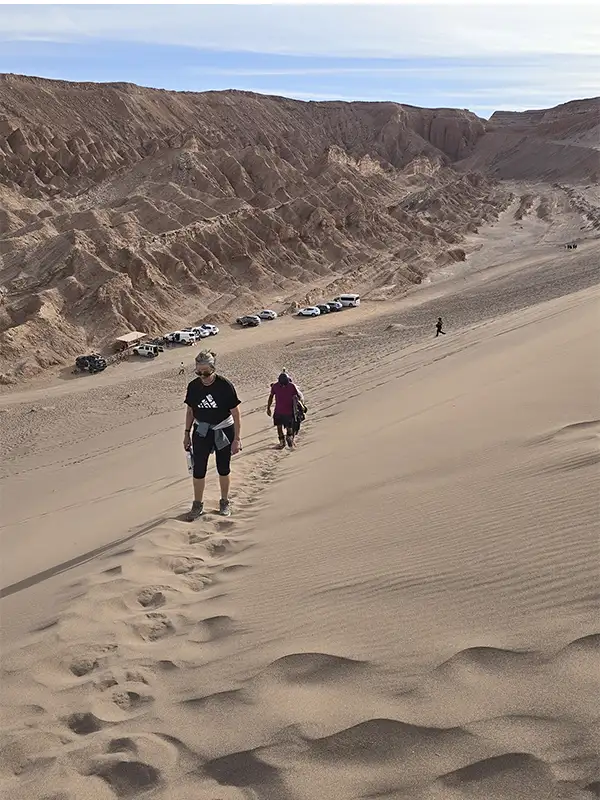 Mujeres descendiendo la Duna Mayor en el Valle de la Muerte con el paisaje desértico de Atacama de fondo