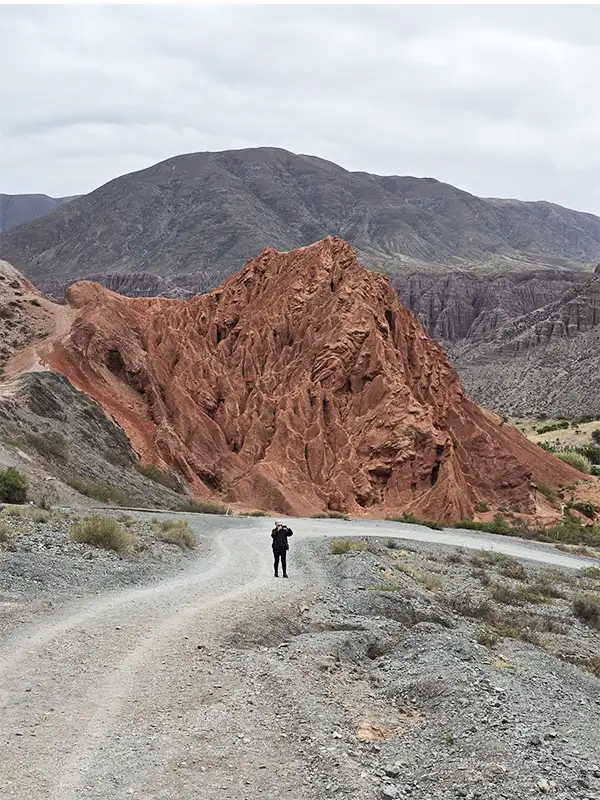 Persona observando las formaciones rojizas de Los Colorados en Purmamarca desde un camino de tierra