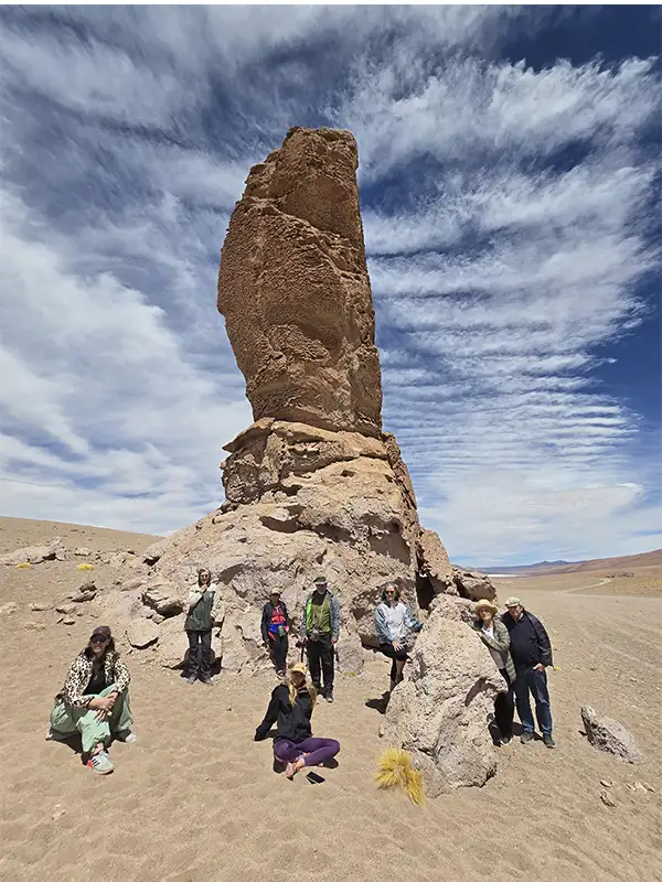 Grupo de viajeros posando junto a uno de los Monjes de Pacana, formación rocosa vertical gigante en el desierto de Atacama