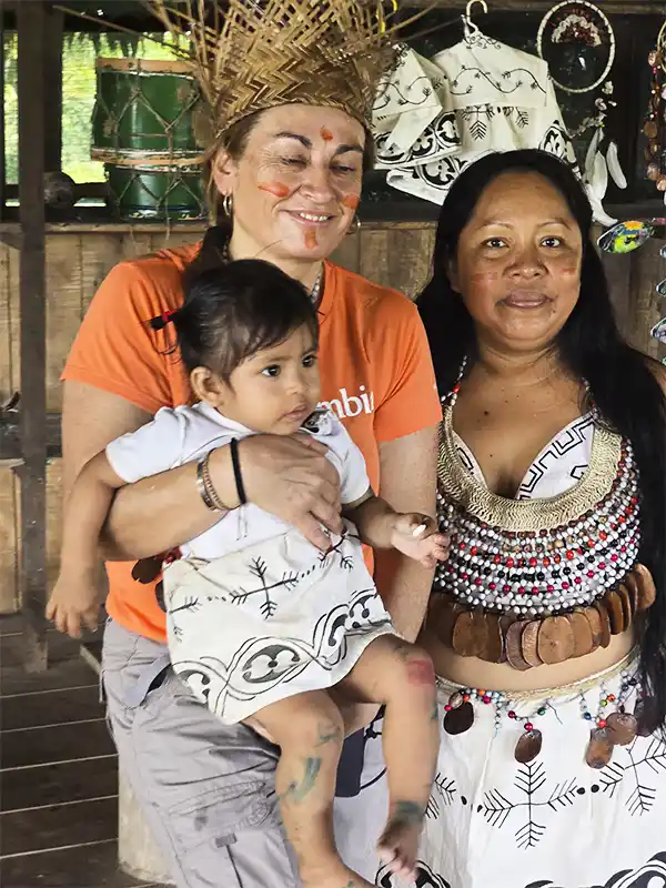 Mujer indígena amazónica junto a una viajera y un bebé, con vestimenta y adornos tradicionales, en una comunidad nativa de Iquitos, Perú.