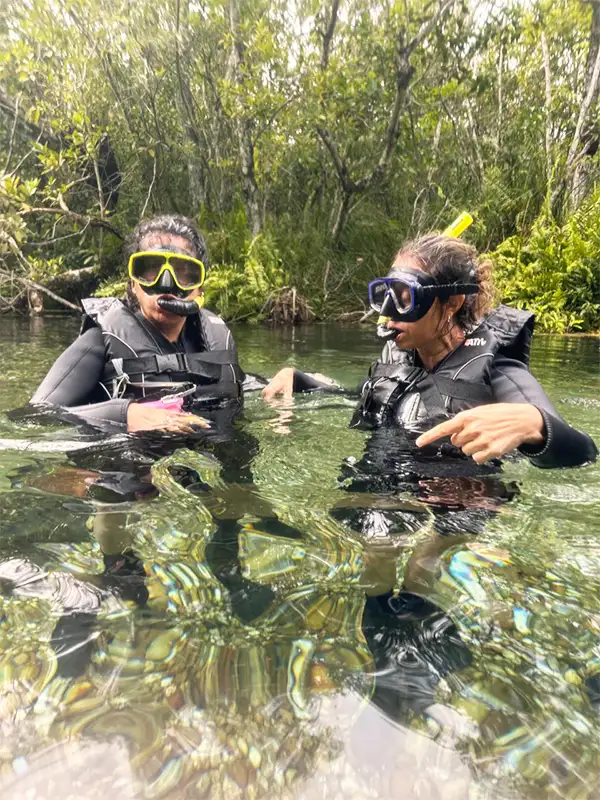 Dos mujeres con equipo de snorkel conversando dentro de un río de Bonito rodeado de selva