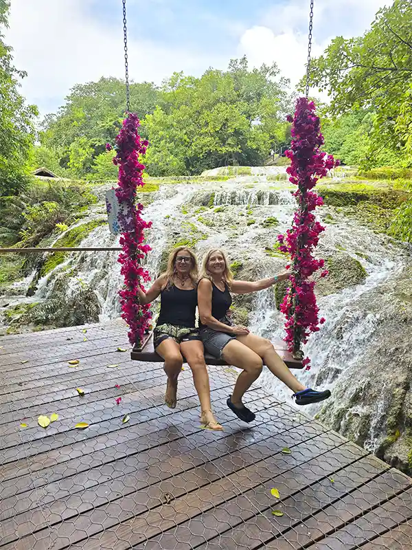 Dos mujeres en una hamaca colgante con flores rosas frente a una cascada en Bonito, Brasil