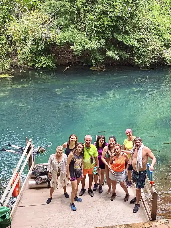 Grupo de viajeros posando en un muelle de madera junto a un río cristalino en Bonito