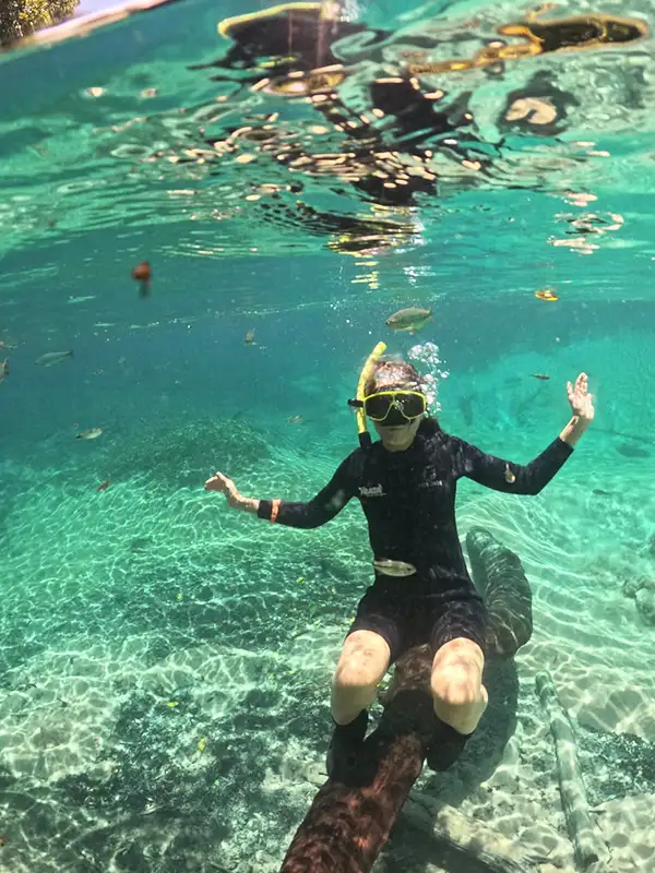 Persona haciendo flotación con snorkel sobre un tronco sumergido en las aguas cristalinas del Río da Prata, Bonito