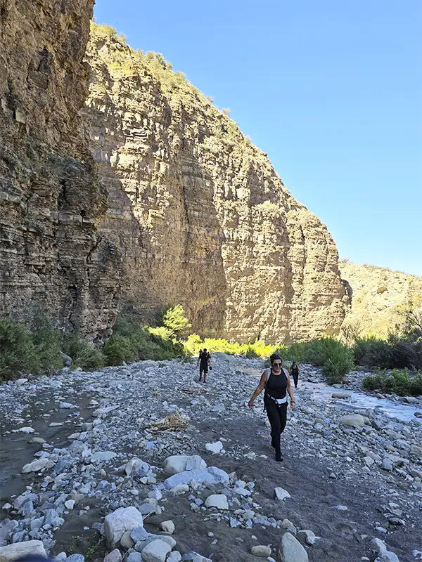 Viajeros cruzando el arroyo entre paredes rocosas durante el trekking en Pasleam