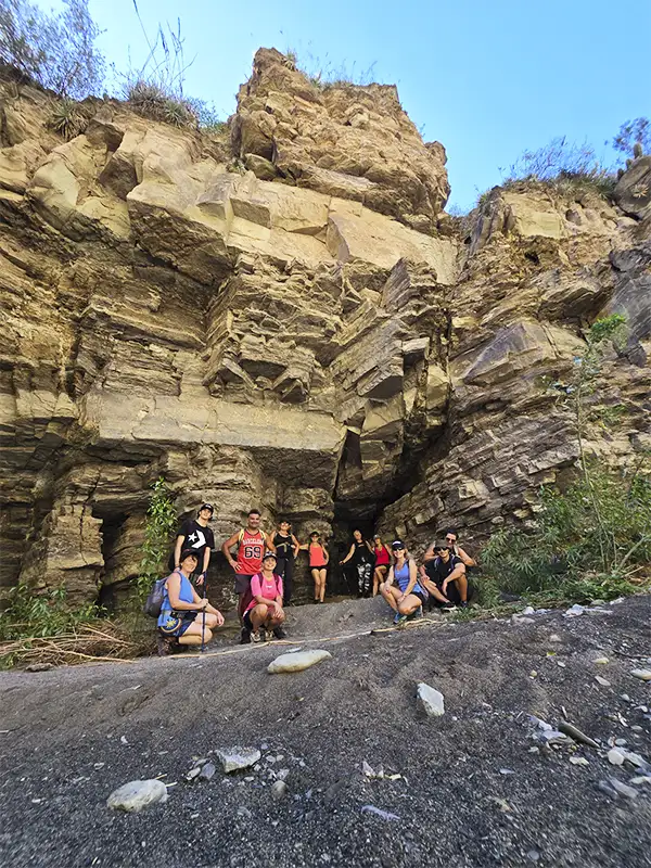 Grupo de viajeros posando frente a formaciones rocosas en el ingreso a una cueva natural, Pasleam